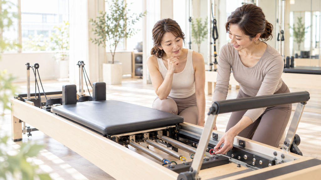 マシンピラティスのスプリングについて説明を受ける女性